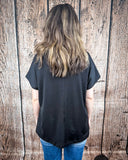 The Thatcher Top in black being styled and modeled by a women in front of a wood background.