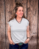 The Sloan Top in Pearl Grey being styled and modeled on a women in front of wood background.