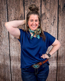 The Thatcher Top in navy being styled and modeled on a women in front of wood background.