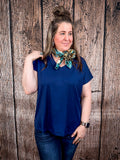 The Thatcher Top in navy being styled and modeled on a women in front of wood background.
