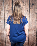 The Thatcher Top in navy being styled and modeled on a women in front of wood background.