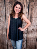 The Caldera Tank in Black being styled with jeans and modeled by a women in front of wood backdrop.