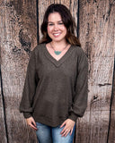 The Hadley Top in mocha being styled with jeans and worn by a women in front of wood background.