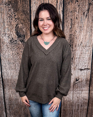 The Hadley Top in mocha being styled with jeans and worn by a women in front of wood background.