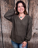 The Hadley Top in mocha being styled with jeans and worn by a women in front of wood background.