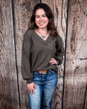 The Hadley Top in mocha being styled with jeans and worn by a women in front of wood background.