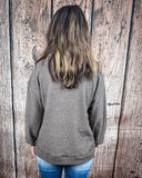 The Hadley Top in mocha being styled with jeans and worn by a women in front of wood background.
