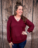 The Hadley Top in wine being styled and worn by a women in front of wood background.