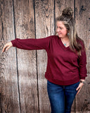 The Hadley Top in wine being styled and worn by a women in front of wood background.