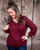 The Hadley Top in wine being styled and worn by a women in front of wood background.