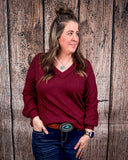 The Hadley Top in wine being styled and worn by a women in front of wood background.