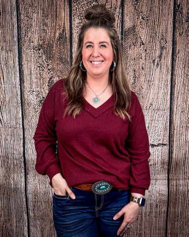 The Hadley Top in wine being styled and worn by a women in front of wood background.