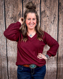 The Hadley Top in wine being styled and worn by a women in front of wood background.
