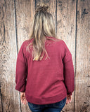 The Hadley Top in wine being styled and worn by a women in front of wood background.