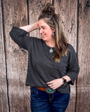 The Ellis Top in black being styled and modeled on women in front of wood background.