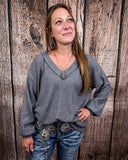 The Hadley Top in Charcoal being styled with jeans and worn by a women in front of wood background.