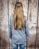 The Hadley Top in Charcoal being styled with jeans and worn by a women in front of wood background.