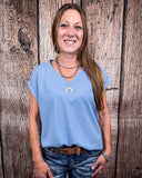 The Sloan Top in denim blue being styled with jeans and worn on women in front of wood background.