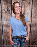 The Sloan Top in denim blue being styled with jeans and worn on women in front of wood background.