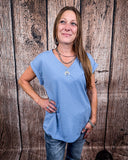 The Sloan Top in denim blue being styled with jeans and worn on women in front of wood background.
