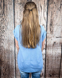 The Sloan Top in denim blue being styled with jeans and worn on women in front of wood background.