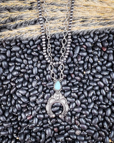Jericho Layered Squash Blossom Necklace being displayed on black pebbles and wheat background.