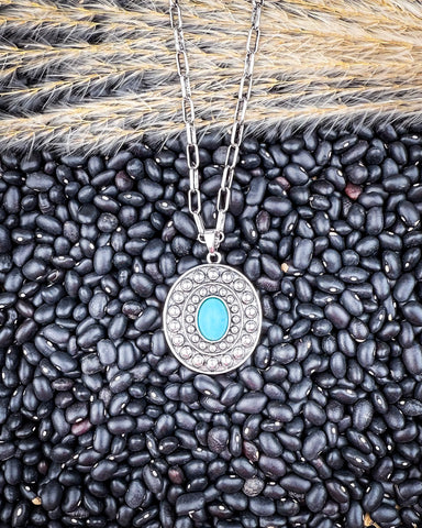 Hobbs Pendant Fashion Necklace being displayed on black pebbled and wheat background.