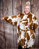 Cow Print Hooded Blanket being worn by a women in front of wood background.