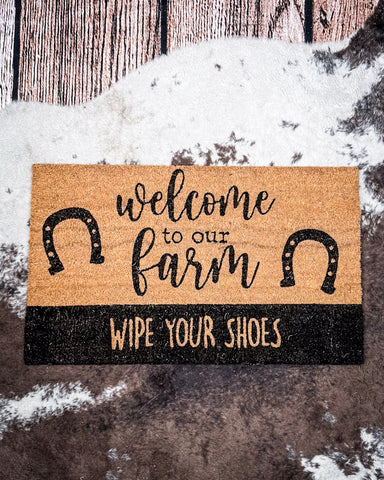 Welcome to Our Farm Coir Doormat displayed on cowhide.