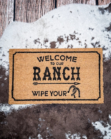 Welcome to Our Ranch Coir Doormat displayed on cowhide.