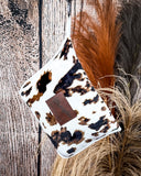 Wrangler Tri-Color Cowhide Travel Blanket displayed in front of wood and wheat background.