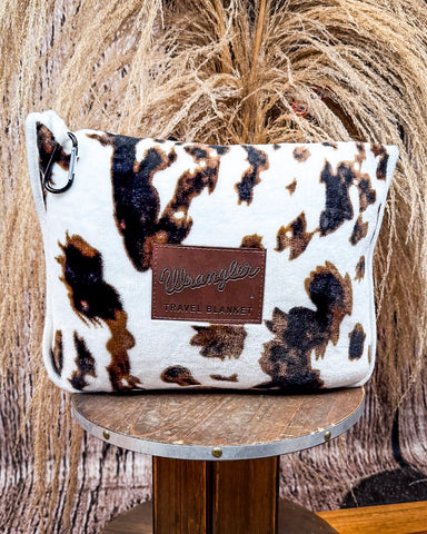 Wrangler Tri-Color Cowhide Travel Blanket displayed on wood table in front of wheat background.