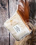 The Cactus Stripe Travel Blanket, hanging from a hook on a wooden backdrop beside wheat.