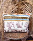 Back view of the bagged Cactus Stripe Travel Blanket on a wooden table with wheat behind it. 