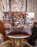 The Westin Hair on Hide Tote Bag on a wooden table with wheat in the background.