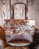Back view of the Westin Hair on Hide Tote Bag on a wooden table with wheat in the background.