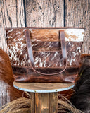 The Westin Hair on Hide Tote Bag on a wooden table with wheat in the background, wood backdrop.