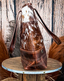 Side view of the Westin Hair on Hide Tote Bag on a wooden table with wheat in the background.