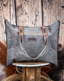 Back view of the Black Sands Weekender Bag on a wooden table with wheat in the background.