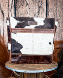 The Salt Creek Hair on Hide Crossbody Bag displayed on a wooden table in a wood backdrop.