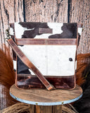 The Salt Creek Hair on Hide Crossbody Bag displayed on a wooden table in a wood backdrop.