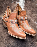 Side view of the  Western Ember Booties in Canyon Brown displayed on cowhide. 
