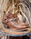 The Western Ember Booties in Canyon Brown on a wooden table with wheat in the background.