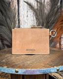 Back view of the of the Wind Rider Card Holder in Brown on a wooden table with wheat in the back.