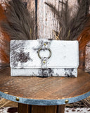 White and black cowhide wallet with brass ring detail on a wooden surface