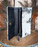 Black and white cowhide leather wallet on a wooden surface with a rustic background