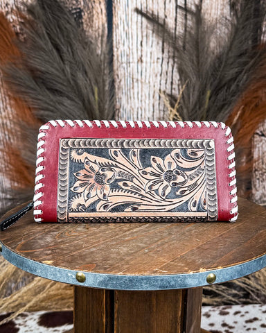 Red leather wallet with floral tooling on a wooden surface