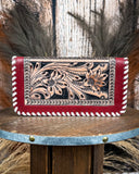 Red leather wallet with floral tooled design on a wooden surface