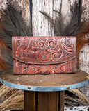 Brown leather wallet with intricate designs on a wooden surface with a rustic background