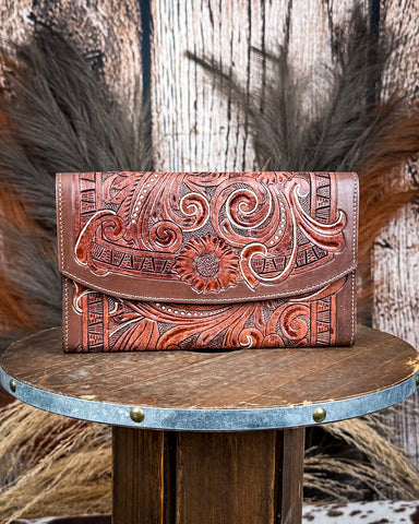Brown leather wallet with intricate designs on a wooden surface with a rustic background